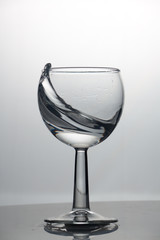 Transparent glass cup with a pouring bubbling cold fresh water with bubbles and drops