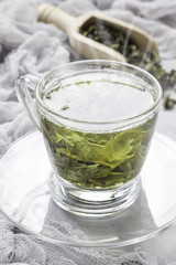 Cup of fresh made hot green tea with smoke, dry leaves on background, vertical