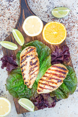 Grilled chicken breast in citrus marinade on salad leaves and wooden cutting board, vertical, top view