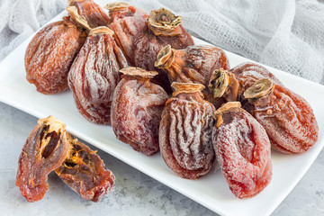 Several dried persimmon on white plate, gray concrete background, horizontal