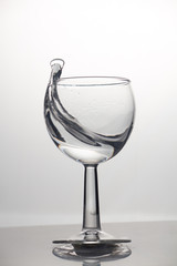 Transparent glass cup with a pouring bubbling cold fresh water with bubbles and drops