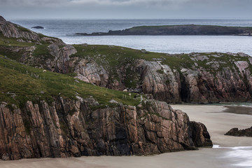 North Coast, Scotland - June 6, 2012: Cliffs descend on Durness Beach, a sandy patch looking north on a rough coast among rock cliffs and sprinkled pieces of rock.