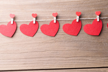 Valentines day concept background.The red heart shape cards and clothespins hanging on rope with retro wood floor background.
