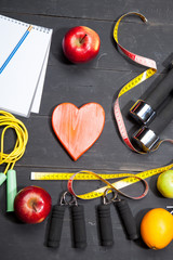 Heart, fruit and dumbbells. Fitness, healthy lifestyle on a black wooden background