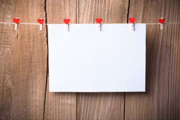 The white greeting card and  heart shape clothespins hanging on rope with old wood floor background.