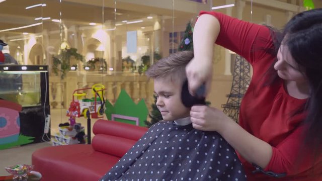 Little boy in hairdressing salon. Barber ending haircutting and hairstyling. Caucasian child sitting on the chair in barbershop.