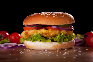 Burger with chicken, salad, cucumbers, tomatoes and onions.