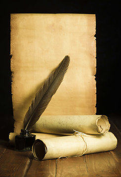 Inkwell with a dark pen, rolls of papyrus on the background of old paper developed