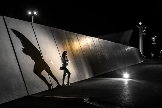 Fototapeta Conceptual photo of silhouette of young woman standing next to the wall at night. There is a big shadow on the wall, Barcelona, Spain