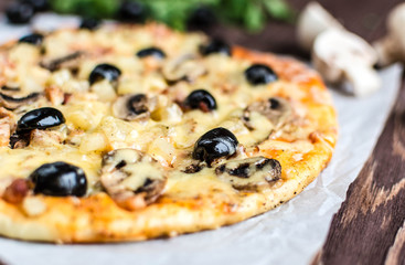 Pizza with meat, mushrooms, pineapple and olives on a wooden background