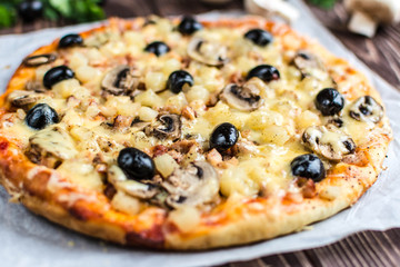 Pizza with meat, mushrooms, pineapple and olives on a wooden background
