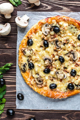 Pizza with meat, mushrooms, pineapple and olives on a wooden background