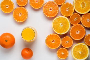 A glass of juice and cut oranges and tangerines on a white backg