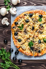 Pizza with meat, mushrooms, pineapple and olives on a wooden background
