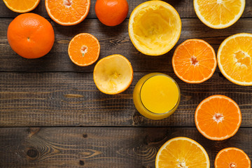A glass of juice and cut oranges and mandarins on the wooden bac