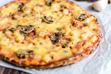 Hawaiian pizza with meat, mushrooms and pineapple on a wooden background