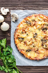 Hawaiian pizza with meat, mushrooms and pineapple on a wooden background