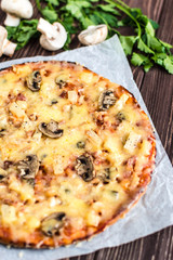 Hawaiian pizza with meat, mushrooms and pineapple on a wooden background