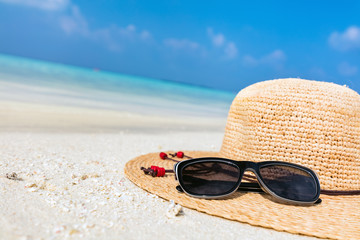 Sun hat and sunglasses on sand, clear turquoise ocean in Maldives.
