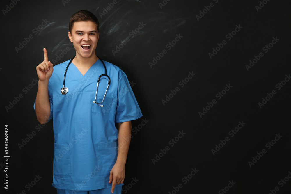 Wall mural Young handsome medical student on blackboard background