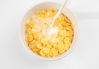 Pouring milk into bowl with corn cereals on white background