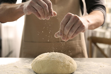 Fototapeta premium Man sprinkling flour over fresh dough on kitchen table