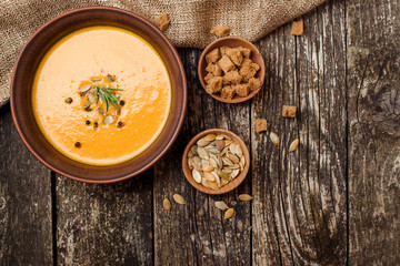 Bowl of pumpkin soup with bread crouton on dark wooden table.