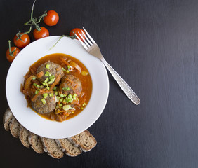 Meatballs in tomato sauce with green onions on a dark background
