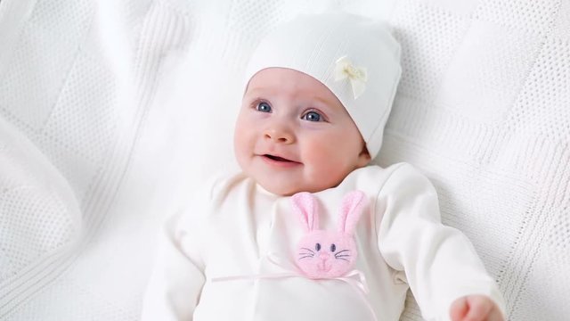 baby girl white knitted jacket with pink rabbit and a white hat lies on bed