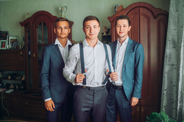 handsome groom posing while stylish groomsman helping him to get ready in the morning. wedding preparation. friends having fun