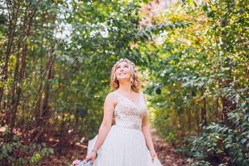 Naklejka premium beautiful bride smiling blonde in the forest holding weddg flowers in hands. Wonderland picture.