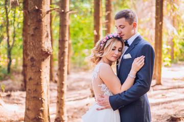 Naklejka premium Just married loving hipster couple in wedding dress and suit on green field in a forest at sunset. happy bride and groom walking running and kissing in the summer meadow. Romantic Married young family