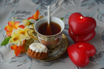 On a wooden table, tea Cup, creamer, flowers in a vase, kettle, marmalade and cakes. Breakfast on Valentine's day - tea, flowers, cake and red candles in the shape of a heart