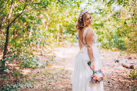 beautiful bride smiling blonde in the forest holding weddg flowers in hands. Wonderland picture.