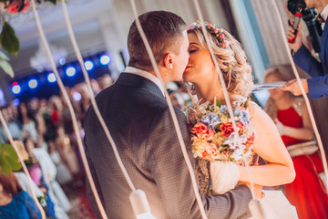 Wedding ceremony. Newlyweds kiss and look at each other under wedding arch. Putting wedding ring on finger.