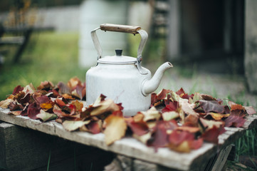 Old rustic aluminum kettle on the damaged wooden table with some autumn leaves as a frame