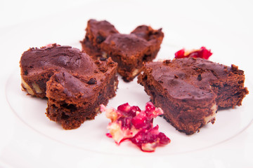 Heart shaped slices of a brownie decorated with pomegranate on white background