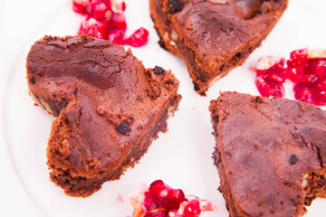 Heart shaped slices of a brownie decorated with pomegranate on white background