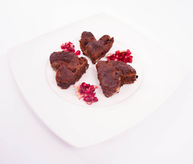 Heart shaped slices of a brownie decorated with pomegranate on white background