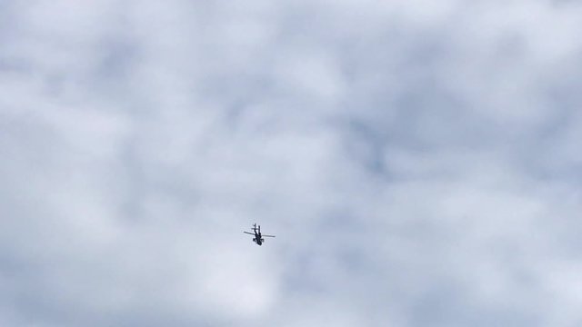 A Military Apache Attack Helicopter flies overhead silhouetted against a cloudy sky