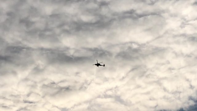 A Military Apache Attack Helicopter flies overhead silhouetted against a cloudy sky