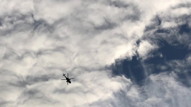 A Military Apache Attack Helicopter flies overhead silhouetted against a cloudy sky