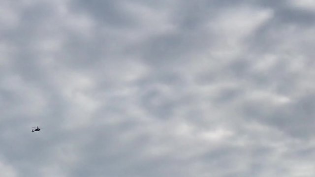 A Military Apache Attack Helicopter flies overhead silhouetted against a cloudy sky