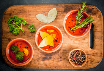 Selection of scented oils from herbs and spices: rosemary, garlic, pepper, parsley, bay leaf. On a dark gray stone kitchen table. Top view, copy space