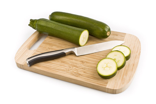 Three green zucchini with cutted pieces on cutting board, isolated on white background. Still-life picture taken in studio with soft-box.