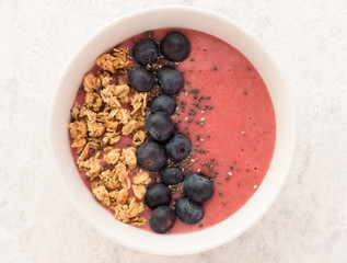 Closeup of a homemade Berry Smoothie with Granola and Blueberries on white textured background.