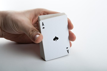 Human hand holding the ace of spades and a deck of cards