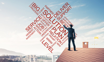 Young businessman standing on house roof and writing leadership 