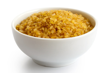 Dry bulgur wheat in white ceramic bowl isolated on white.