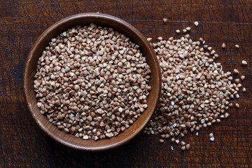 Dry buckwheat in brown wooden bowl isolated on dark wood.